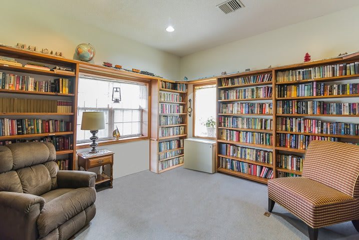 A cozy reading room with bookshelves filled with books, an armchair, and natural light from the windows.