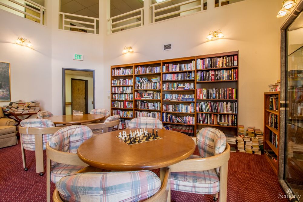 A cozy library with bookshelves filled with books, a round table surrounded by chairs, and a chess set ready for play.