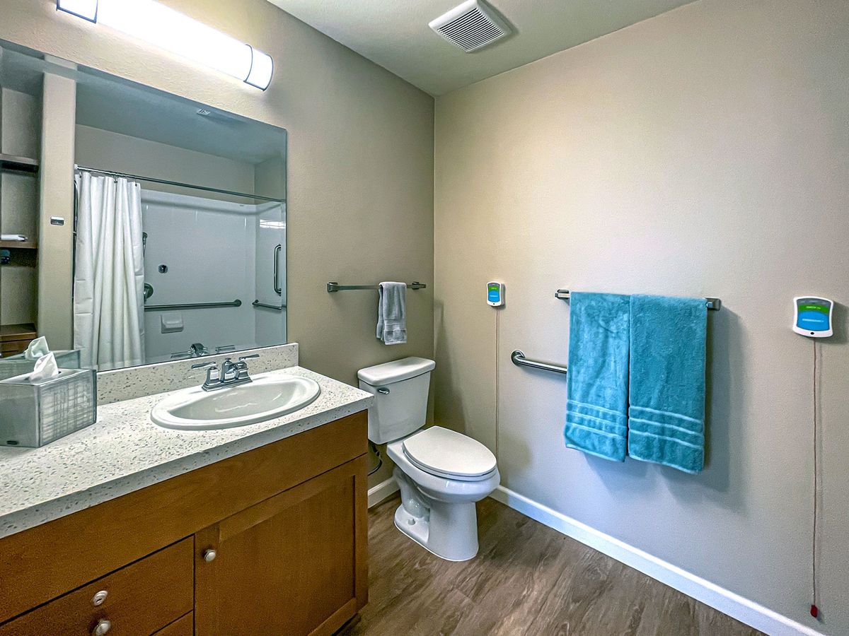 A clean and accessible bathroom with a sink, toilet, mirror, and towel.