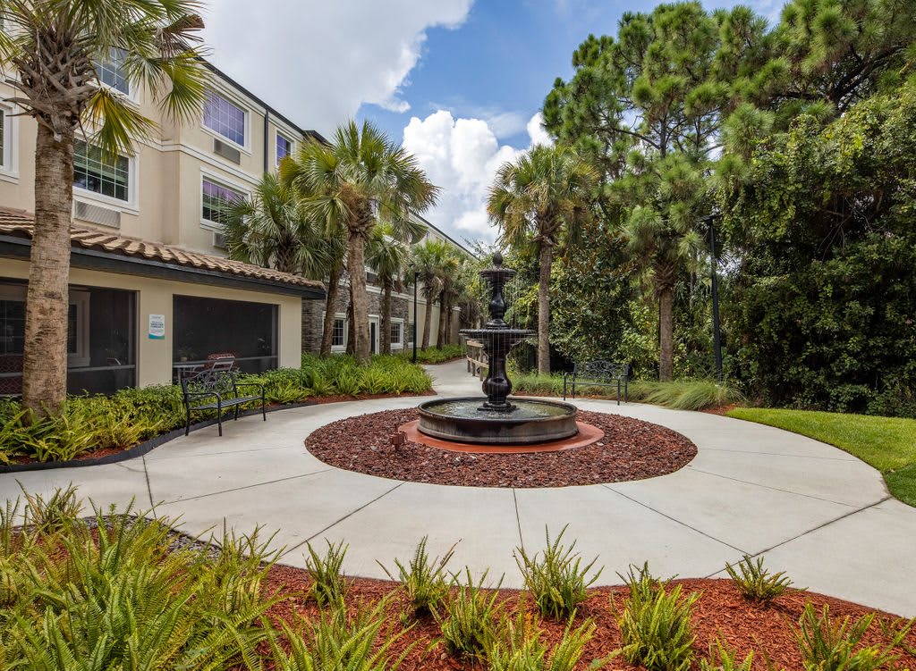 A scenic view of an apartment complex courtyard featuring a central fountain surrounded by palm trees and well-maintained landscaping.