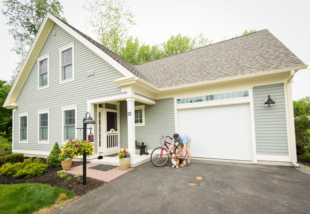 A person interacts with a bicycle and dog outside their house in the driveway.