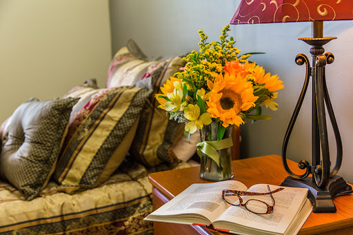 A cozy bedroom corner featuring a vibrant floral arrangement, a book, and reading glasses.