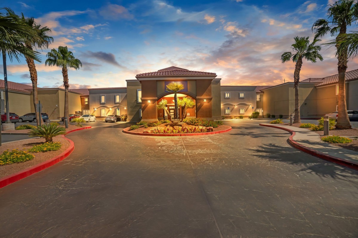 A welcoming hotel entrance at dusk, surrounded by palm trees and illuminated with warm lights.