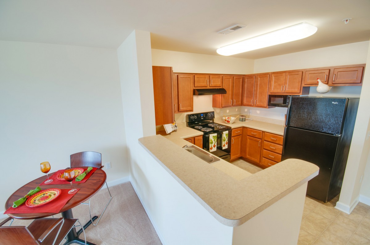 A modern apartment kitchen with wooden cabinets and a small dining area.