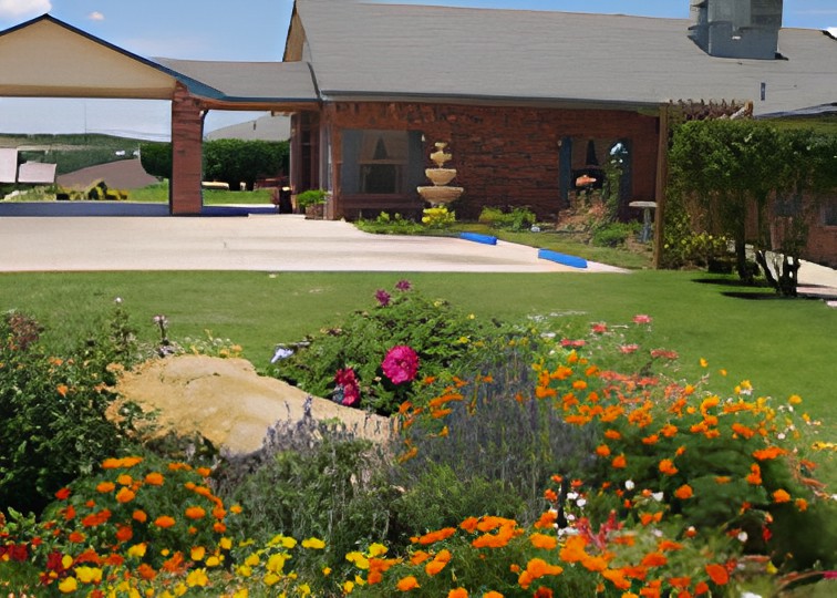A charming brick house with a vibrant garden and fountain in the yard.