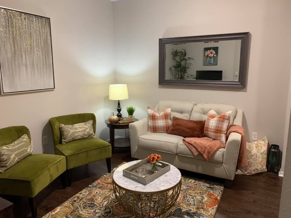 A cozy living room with a white sofa adorned with pillows, a green armchair, and a decorative coffee table, illuminated by a warm lamp.