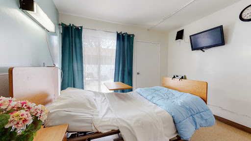 A well-lit hospital room featuring a bed with blue bedding, curtains, and a television.