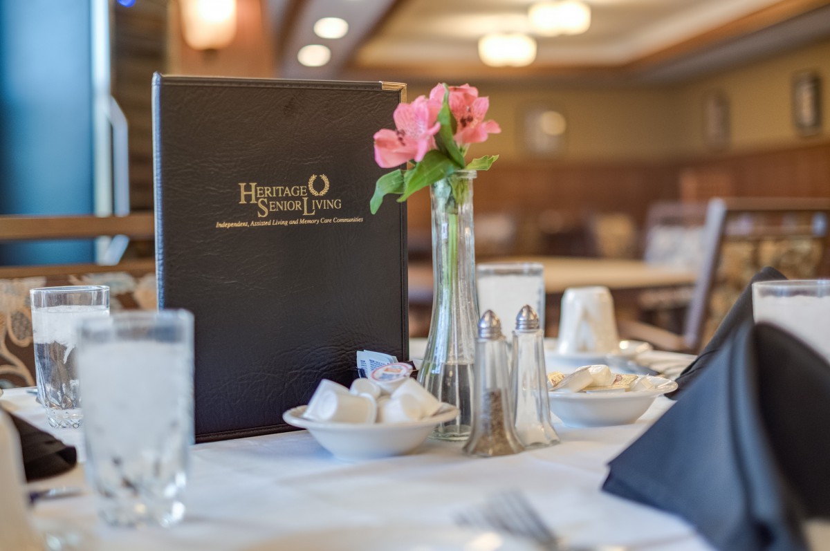 A well-set restaurant table with a menu and flowers.
