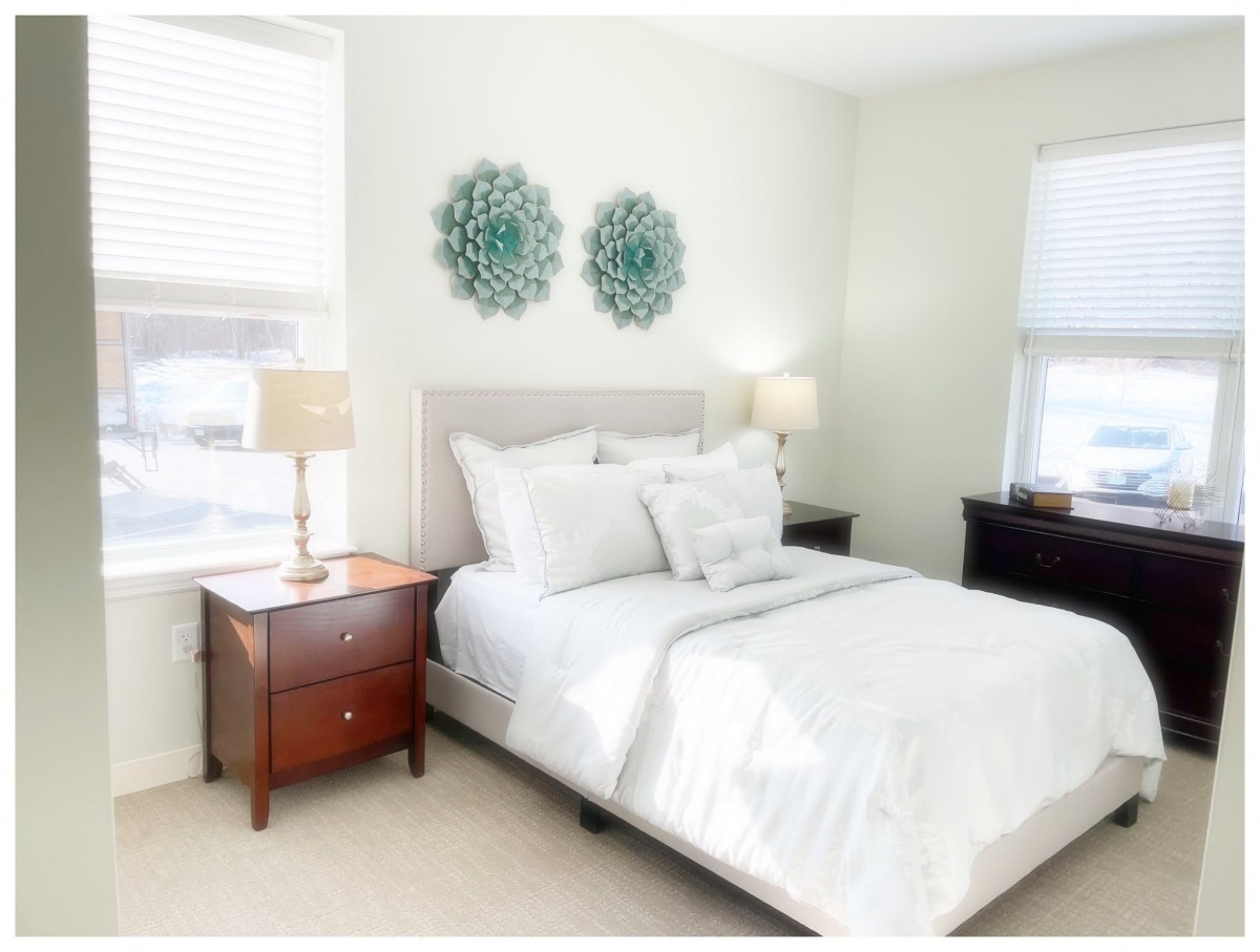 A bright and cozy bedroom with elegant decor, featuring a neatly made bed, bedside tables, lamps, and wall art.