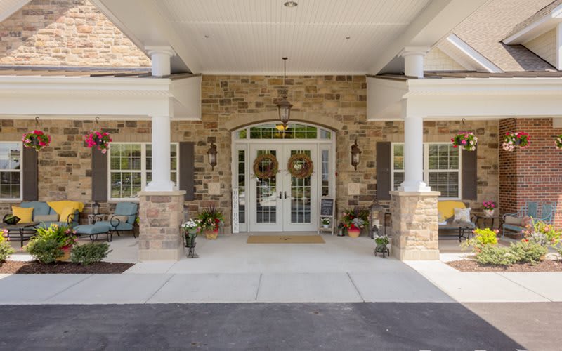 A welcoming front porch with stone facade, columns, and decorative elements like wreaths and potted plants.