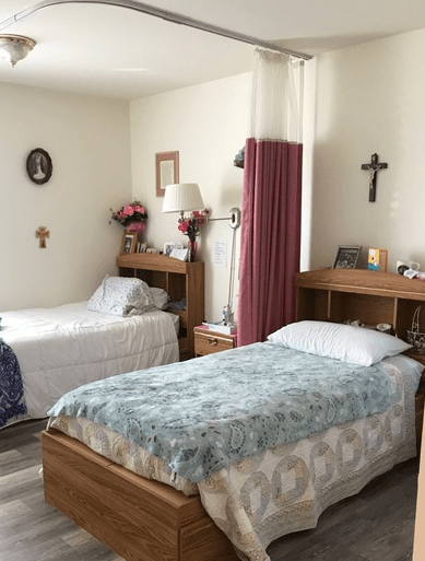 A cozy bedroom with two beds separated by a curtain, featuring religious decor on the walls.