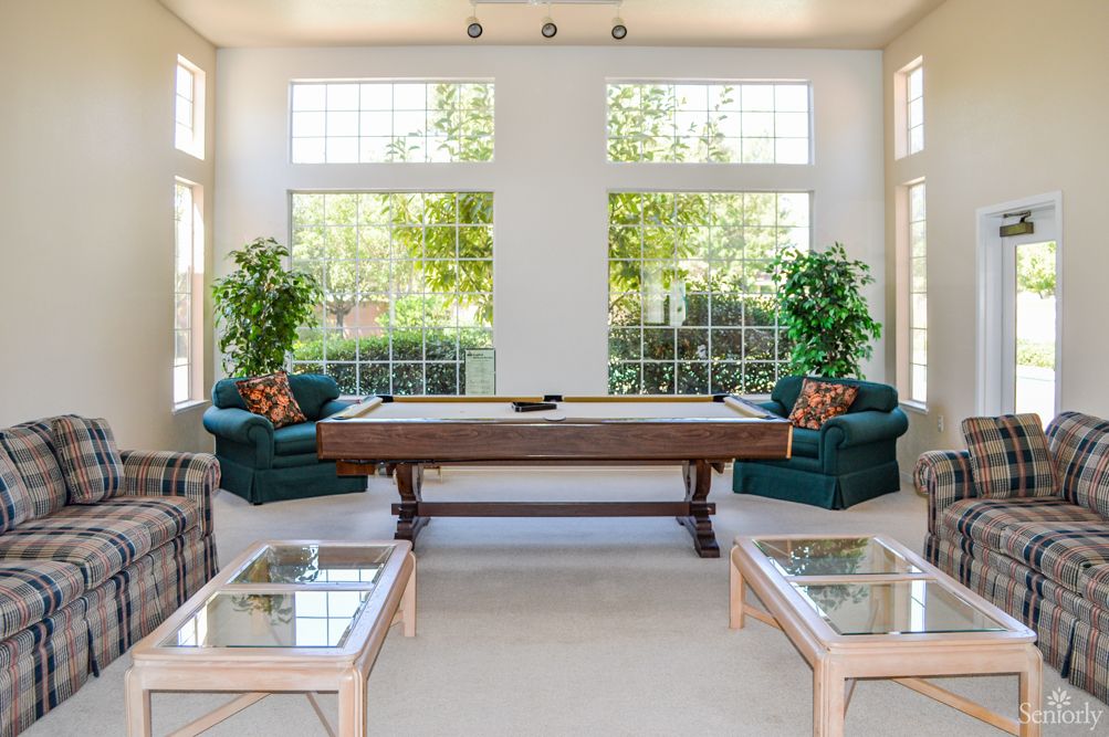 A bright living room featuring a shuffleboard table, large windows, and comfortable seating.