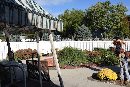 A serene outdoor garden space featuring colorful flowers and green trees, complemented by a striped awning.