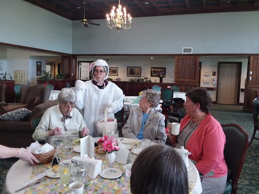 A group of people gathered around a dining table indoors, with a chandelier overhead.