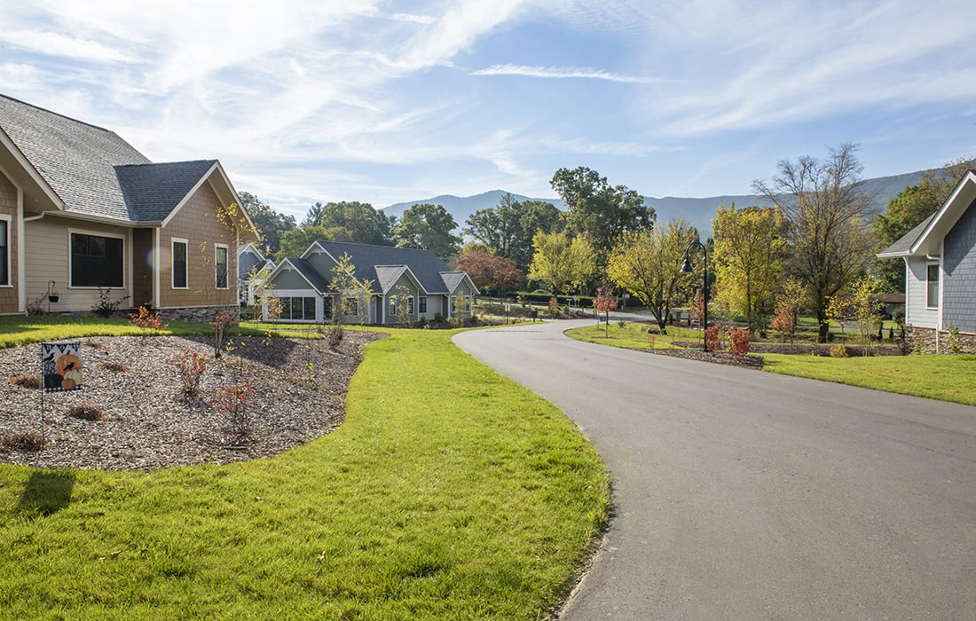 A suburban neighborhood with houses lining a winding road under a clear blue sky.