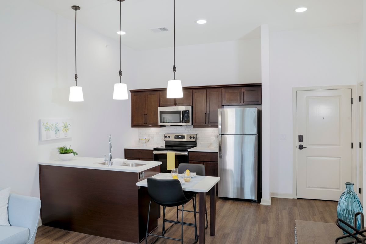 A modern kitchen with stainless steel appliances, dark wooden cabinets, and an island counter featuring pendant lighting.
