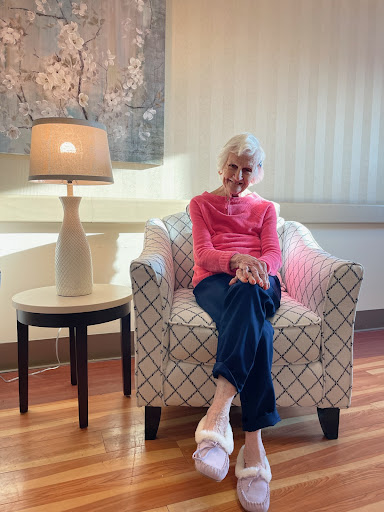 An elderly woman sits comfortably in a stylish chair, enjoying the warm light of a nearby lamp.