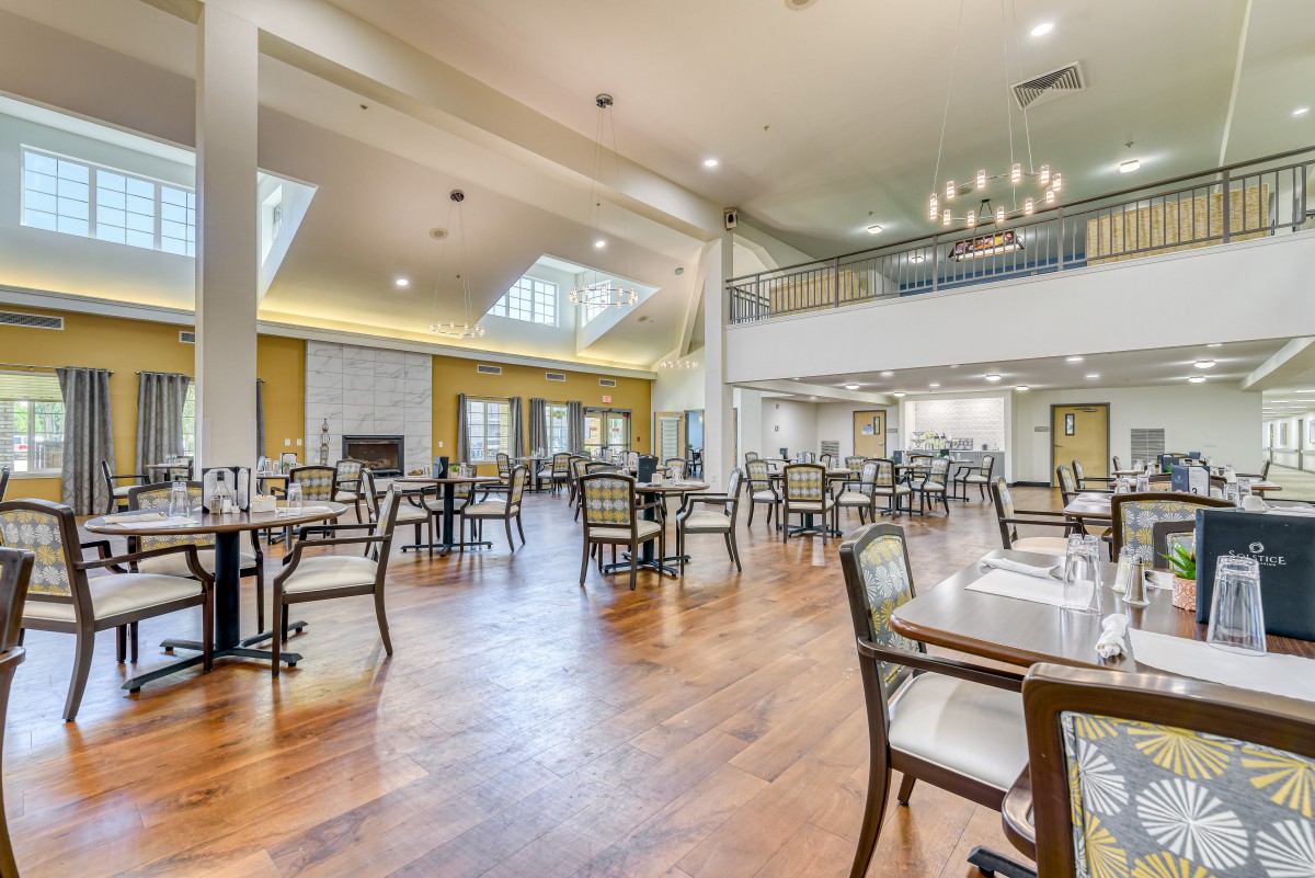A spacious and modern restaurant interior with neatly arranged tables and chairs, featuring a chandelier and wooden flooring.