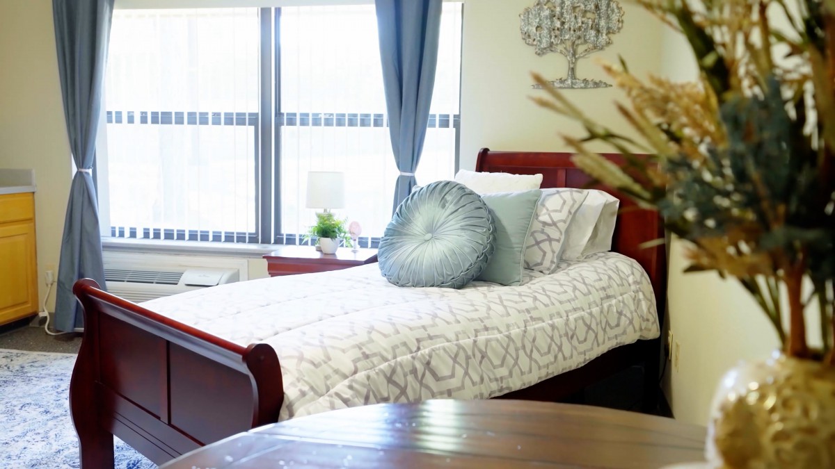 A cozy bedroom with a neatly made bed, decorative pillows, and large windows with curtains.