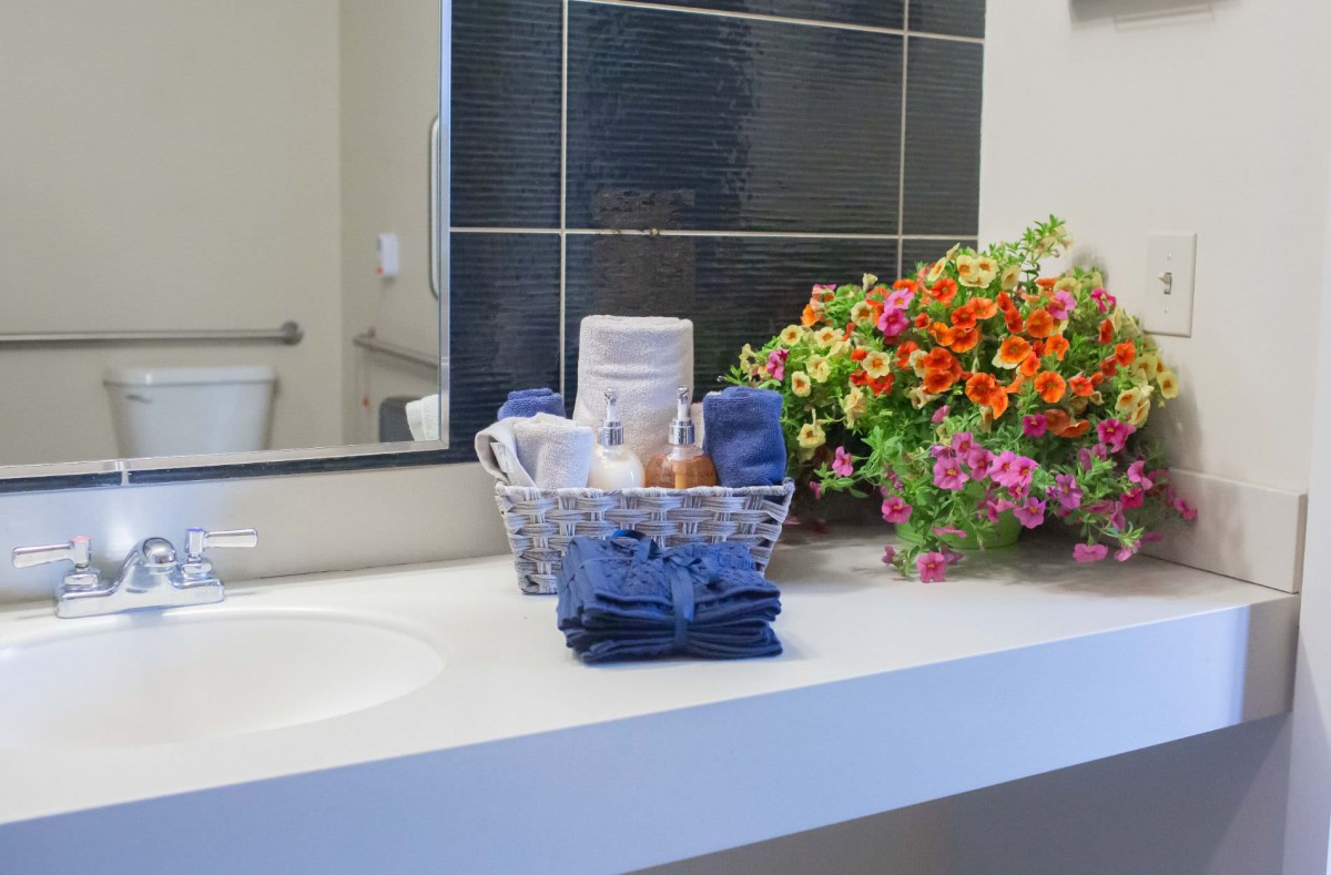 A tidy bathroom counter with neatly arranged towels, toiletries in a basket, and colorful flowers.
