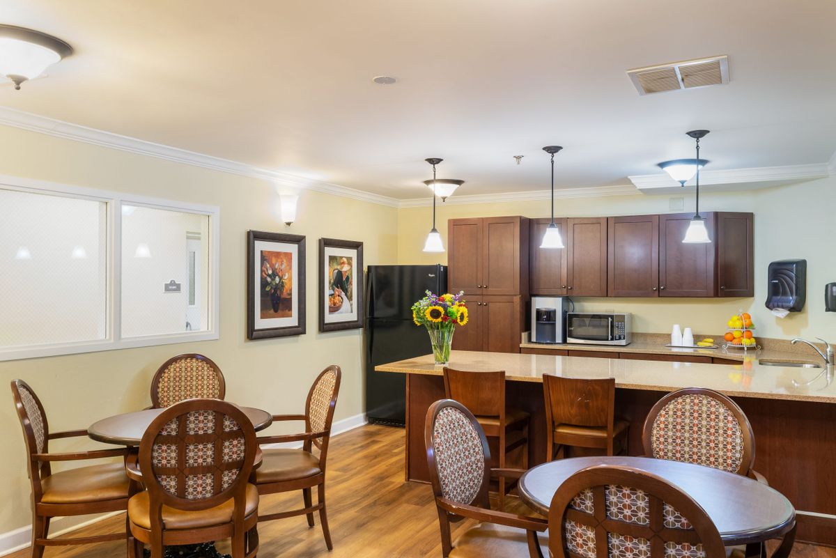 A cozy kitchen and dining area featuring a breakfast bar with bar stools, wooden tables and chairs, and warm lighting.