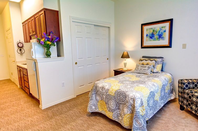 A cozy bedroom with a single bed, adorned with a colorful quilt, a bedside lamp, and a flower vase.