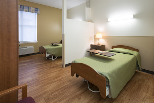 A bright and tidy hospital room featuring two beds with green linens, designed for patient comfort.