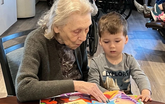 An elderly person and a young child are reading a book together, highlighting intergenerational interaction.