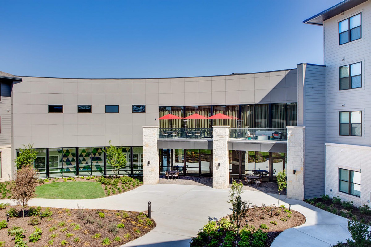 A modern building with large glass windows and well-maintained landscaping, viewed during the daytime.