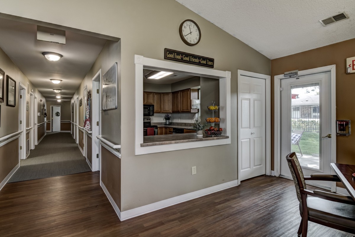 A view of a kitchen and corridor area with a reception window and clock on the wall.