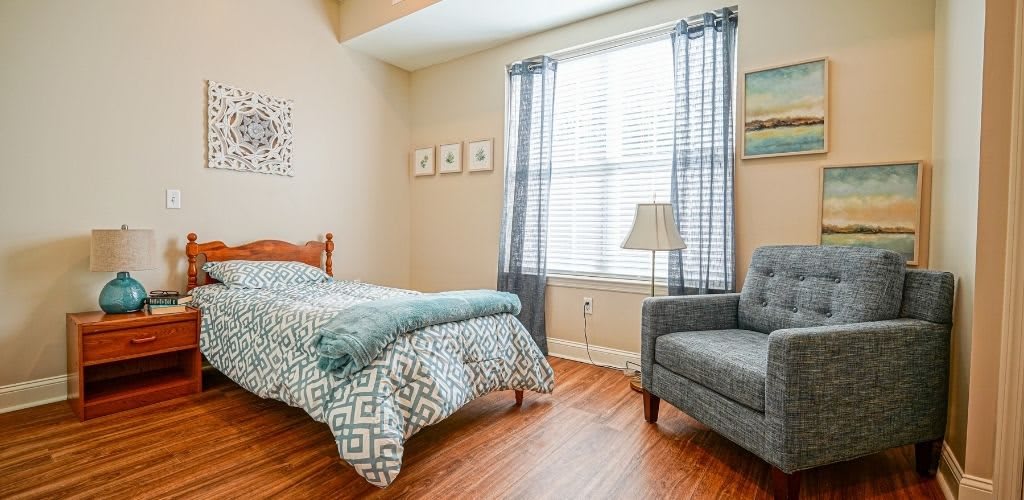 A cozy bedroom with a single bed, armchair, and a window with sheer curtains.