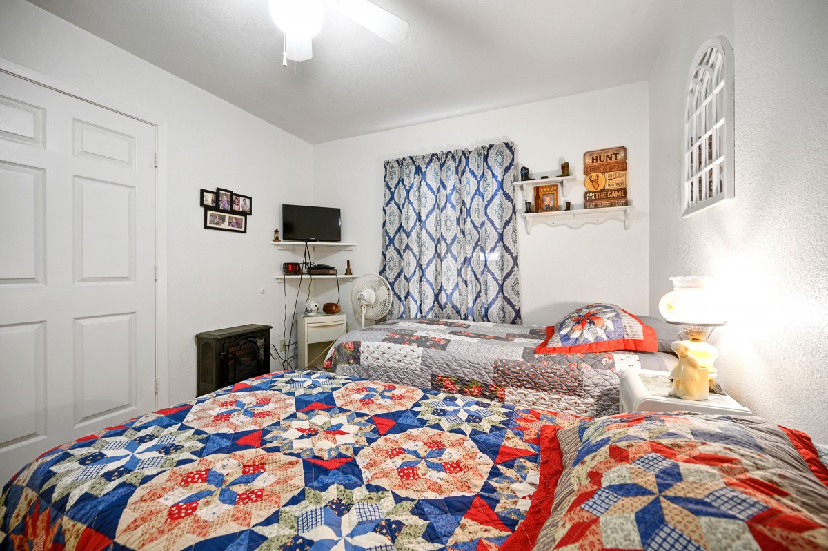 A cozy bedroom featuring colorful quilts and minimal decor with a small TV and shelves.