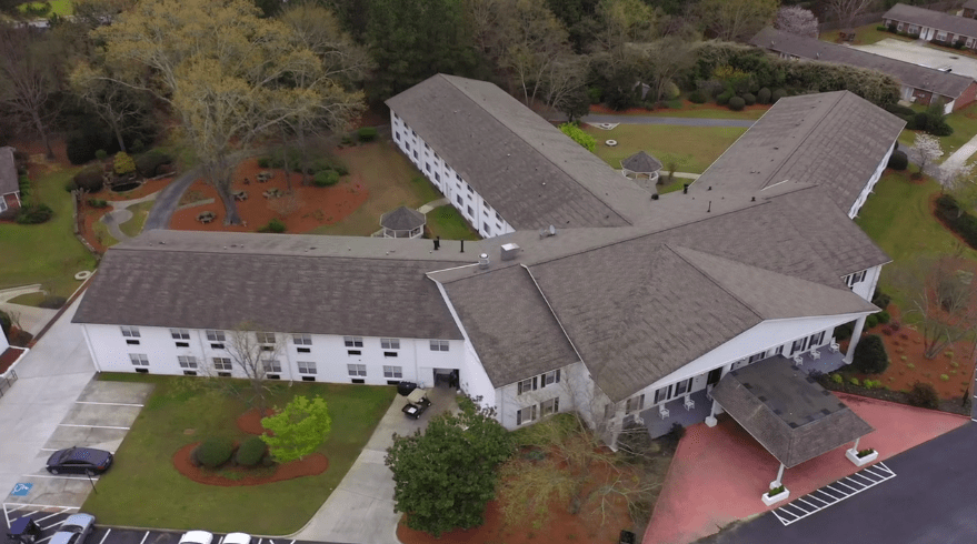 An aerial view of a large building surrounded by trees and a driveway.