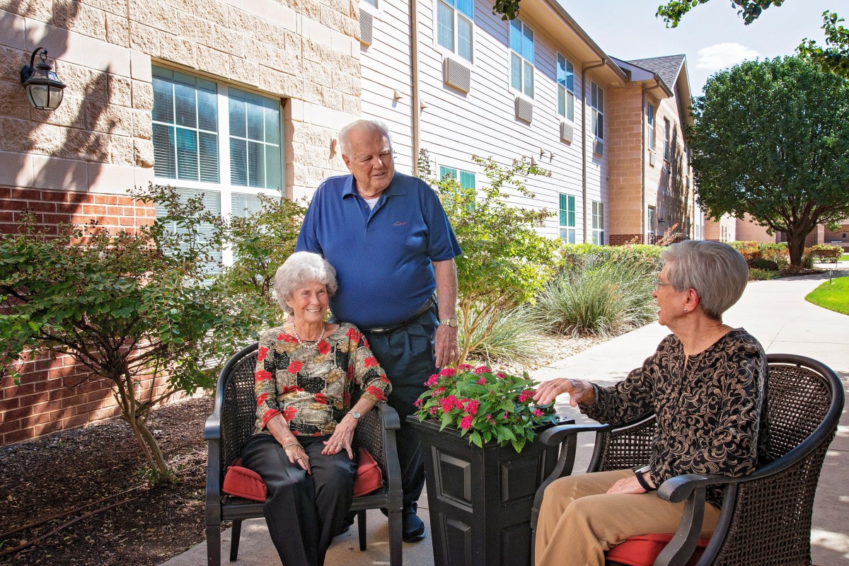 A group of seniors enjoying a conversation outside in a garden setting.