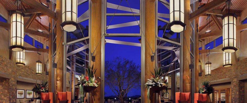 A modern architectural interior with large windows, illuminated by blue lighting and decorated with plants.