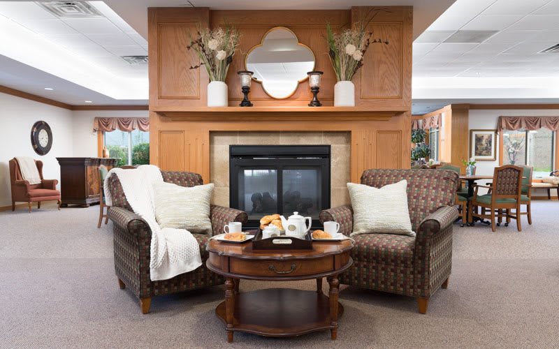 A cozy living room with two armchairs facing a fireplace, adorned by a decorative mirror and vases with plants on the mantel.