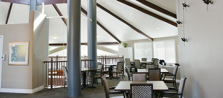 A spacious restaurant interior with tables and chairs arranged neatly under a high ceiling with visible beams.