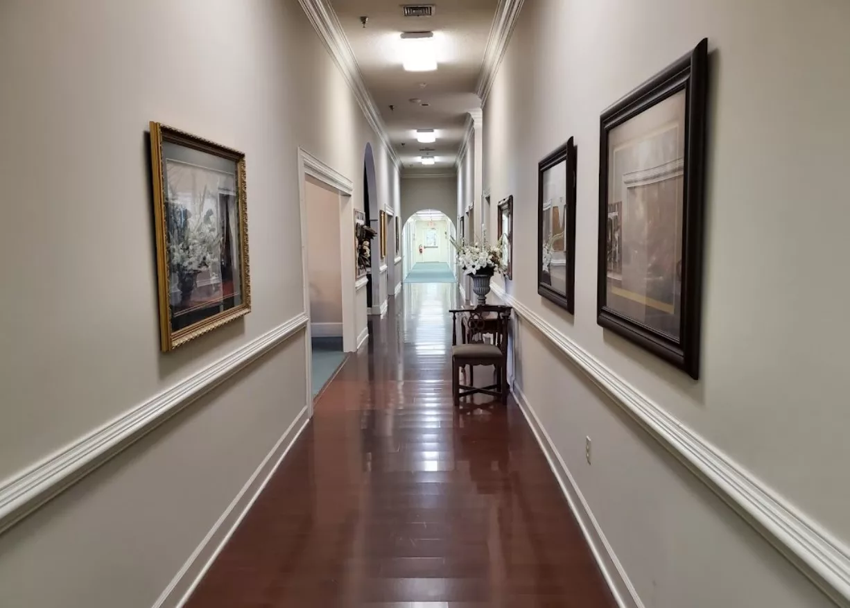 A long hallway featuring wooden flooring and adorned with framed paintings on the walls.