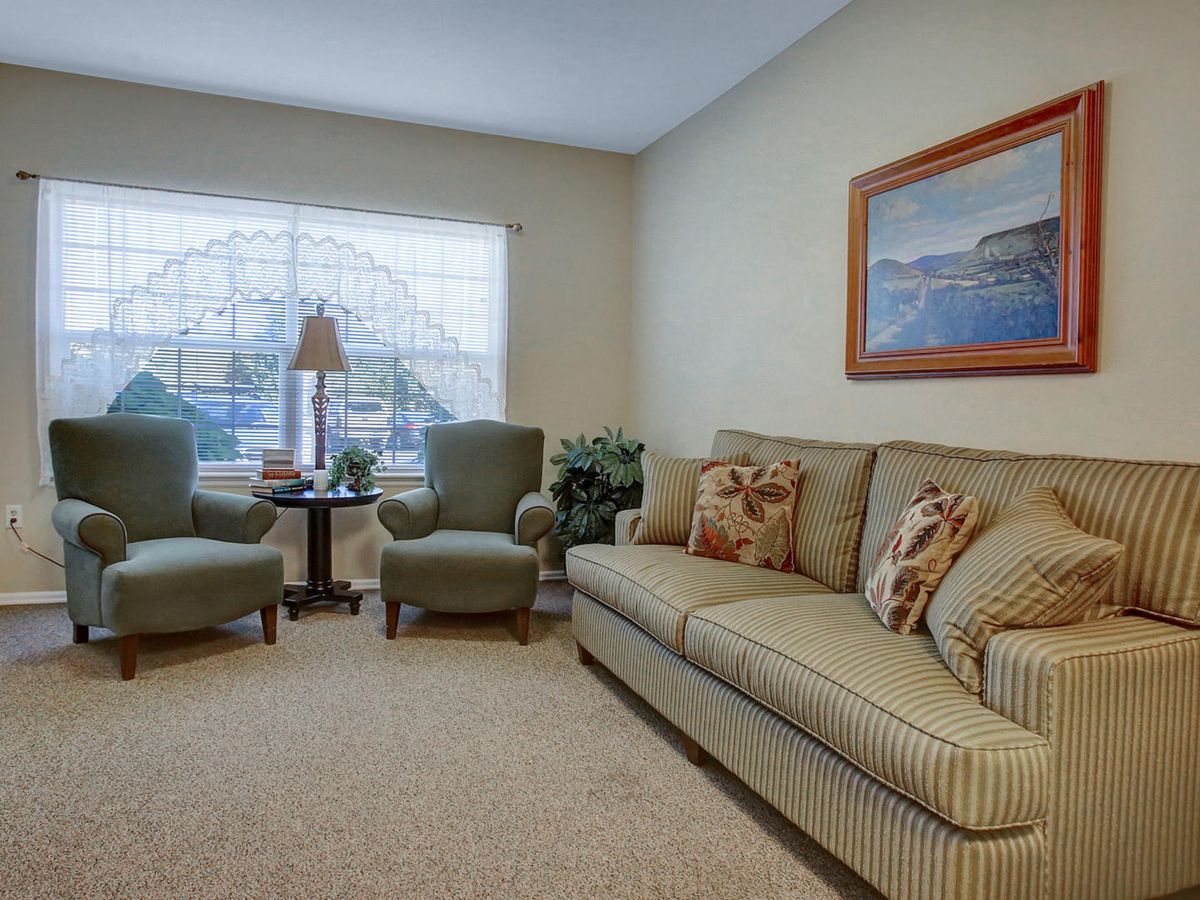 A cozy living room with a sofa, two armchairs, and a large window letting in natural light.