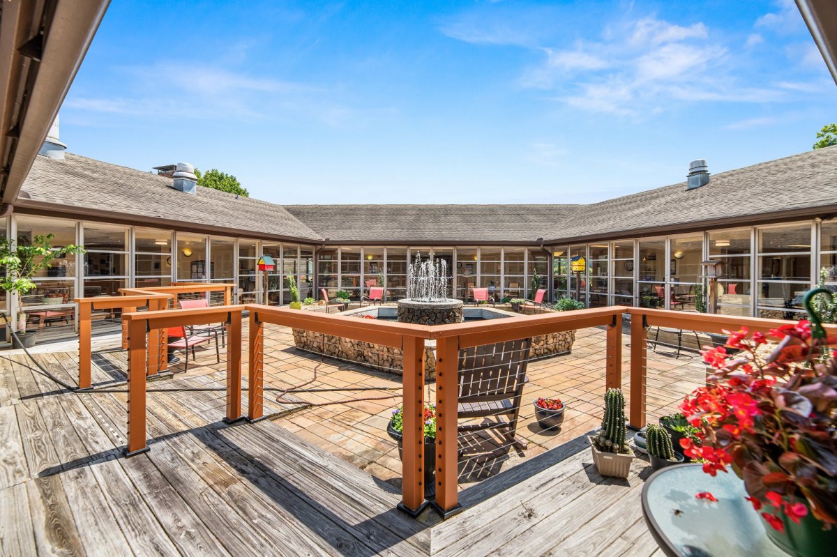 A spacious outdoor patio with a central fountain surrounded by wooden railings on a sunny day.
