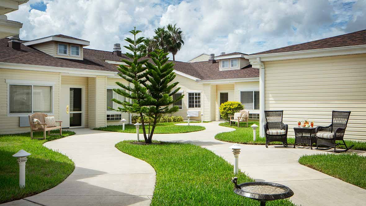 A well-maintained residential courtyard with a pathway, lush grass, and outdoor seating.