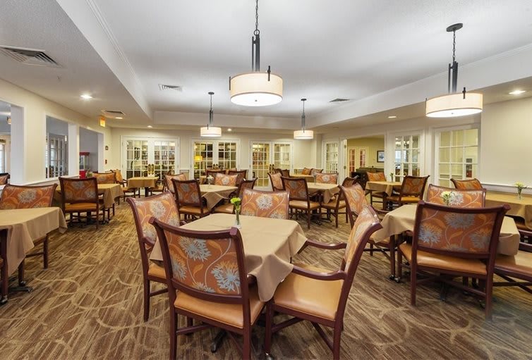 A spacious dining room with elegantly arranged tables and chairs, featuring warm lighting and tasteful decor.