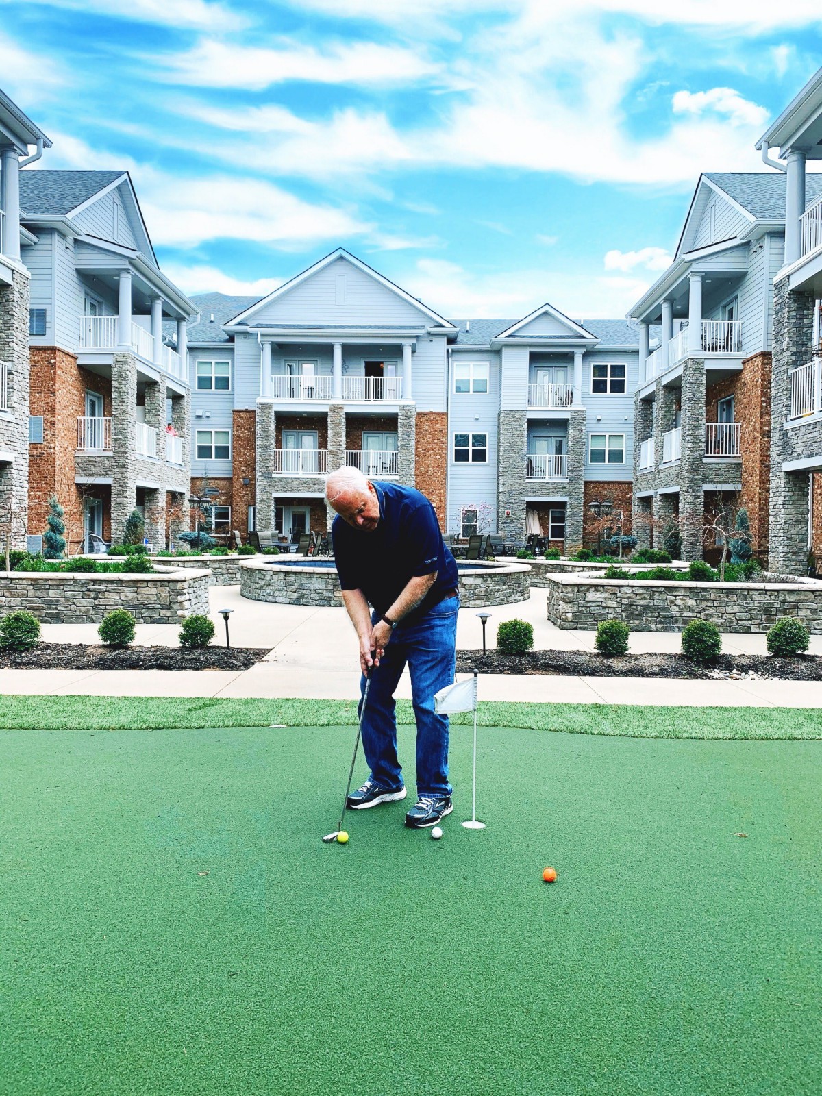 A person practicing putting on a green in front of an apartment complex.