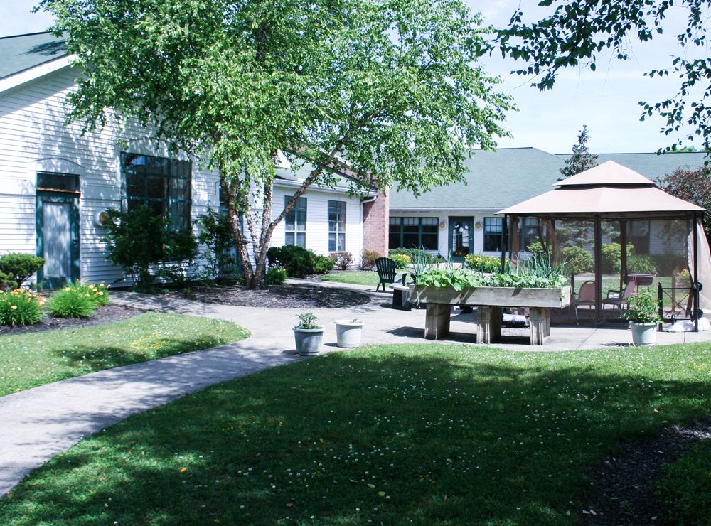 A serene garden with a gazebo, benches, and a pathway surrounded by lush trees and landscaping.