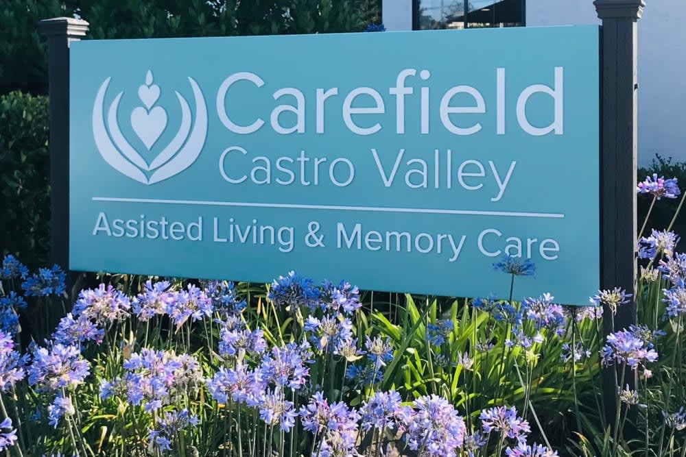 A sign for Carefield Castro Valley Assisted Living & Memory Care, surrounded by blooming flowers.
