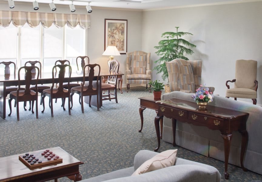 A well-furnished living room with a dining area, featuring elegant chairs, a large window, and decorative elements such as artwork and a potted plant.