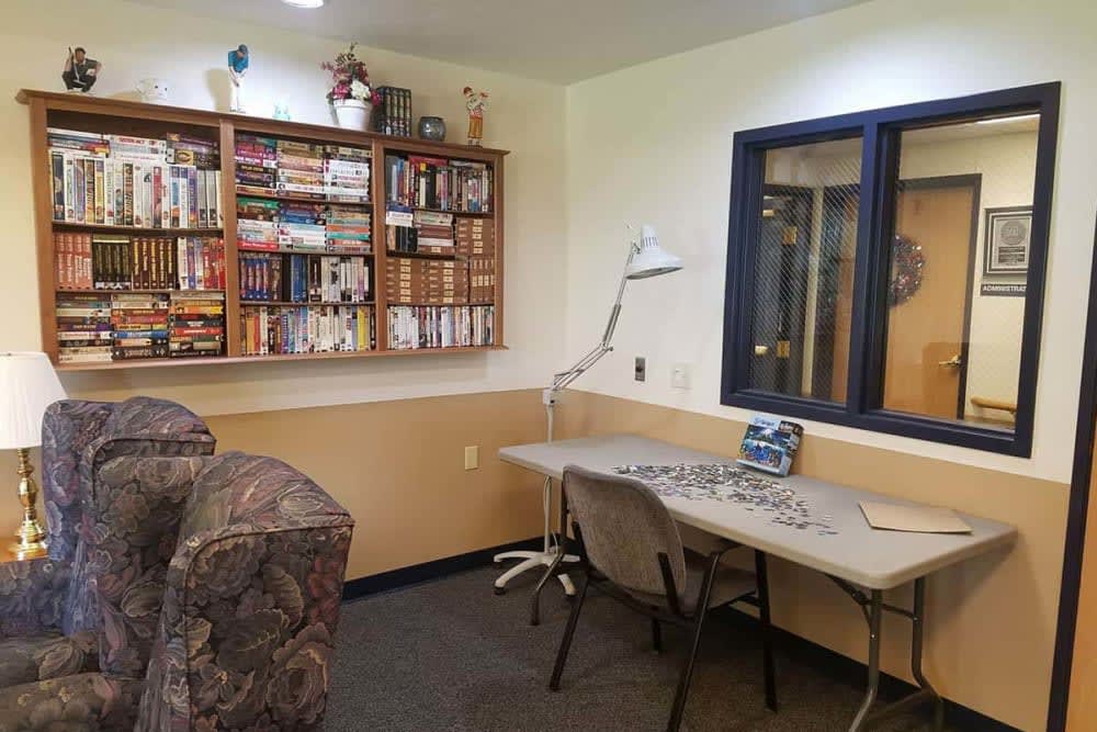 A cozy library corner featuring a bookshelf filled with books, a desk with a lamp, and comfortable seating.