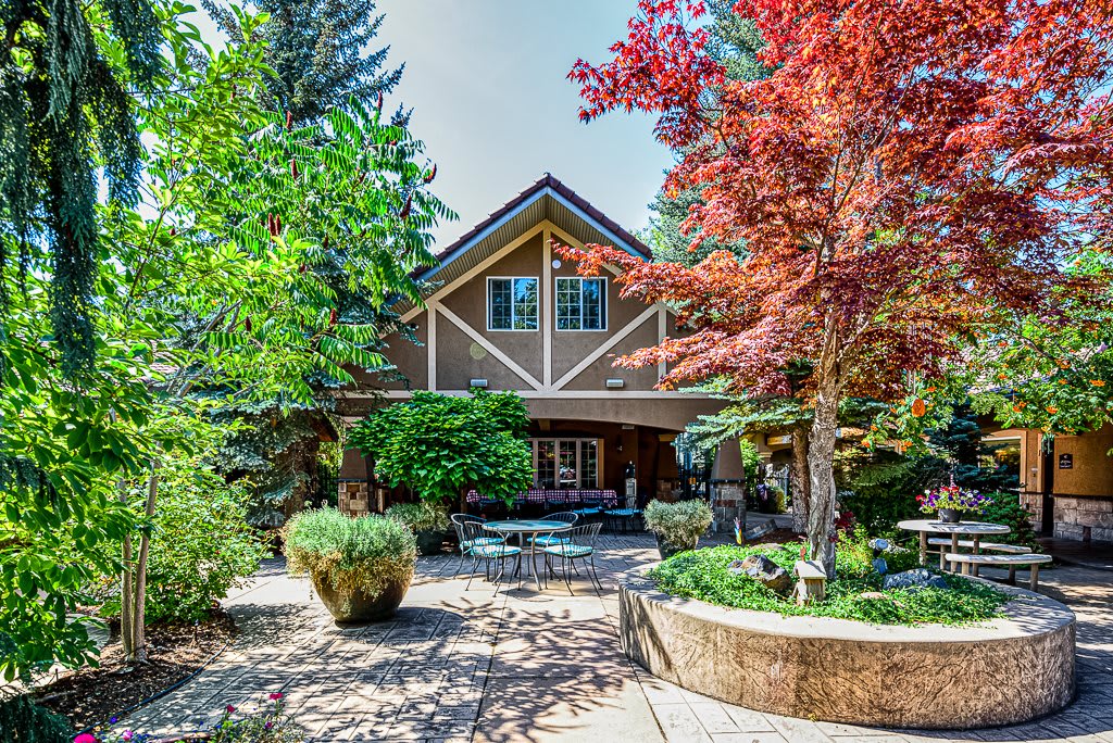 A beautiful house surrounded by a well-maintained garden with colorful trees and a cozy patio area.
