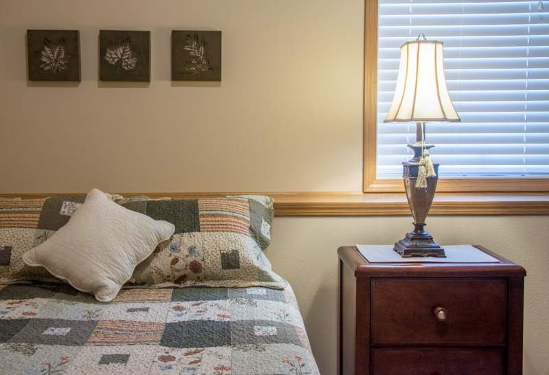 A cozy bedroom with a quilted bedspread, nightstand, and decorative lamp.