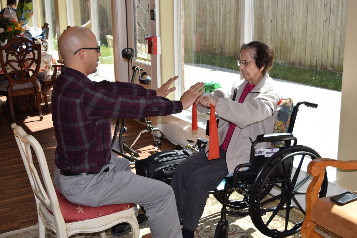 A caregiver assists an elderly person in a wheelchair with physical therapy exercises using resistance bands.